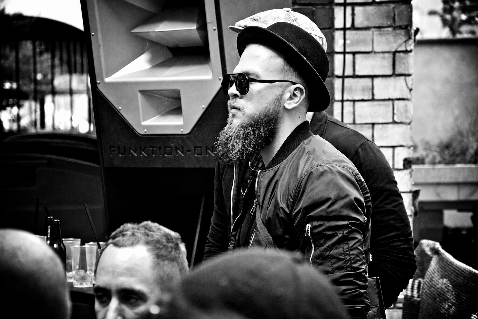 Bearded man with hat and sunglasses beside a Funktion-One soundsystem, black and white