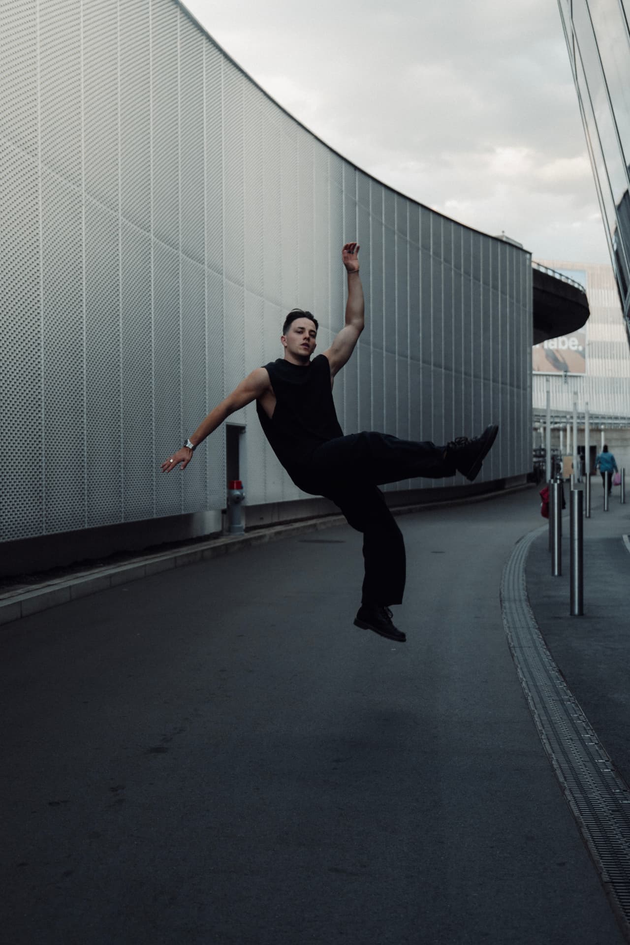 Dancer mid-jump on an empty street beside a curved facade