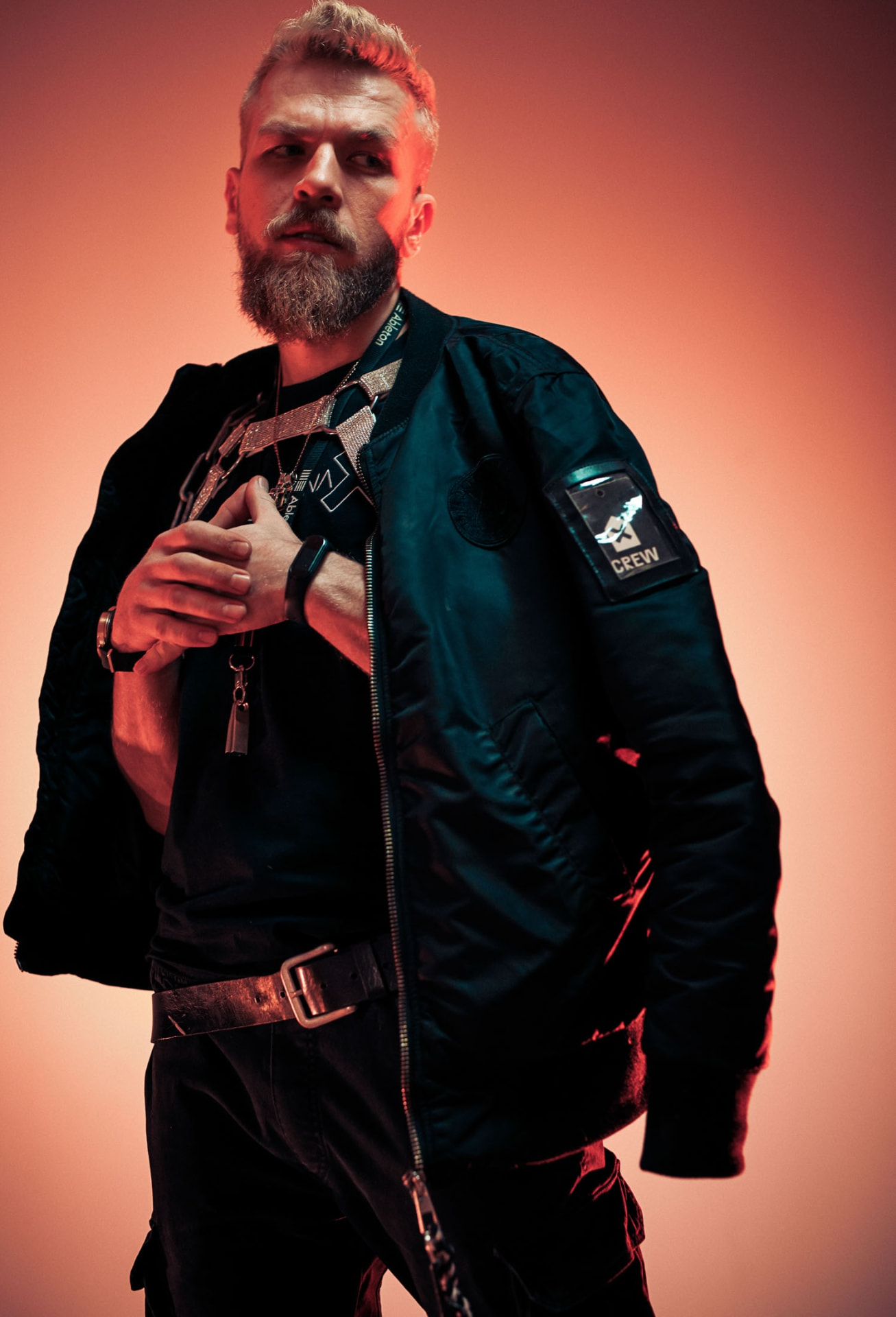 Bearded artist in a black bomber jacket against a warm red studio backdrop