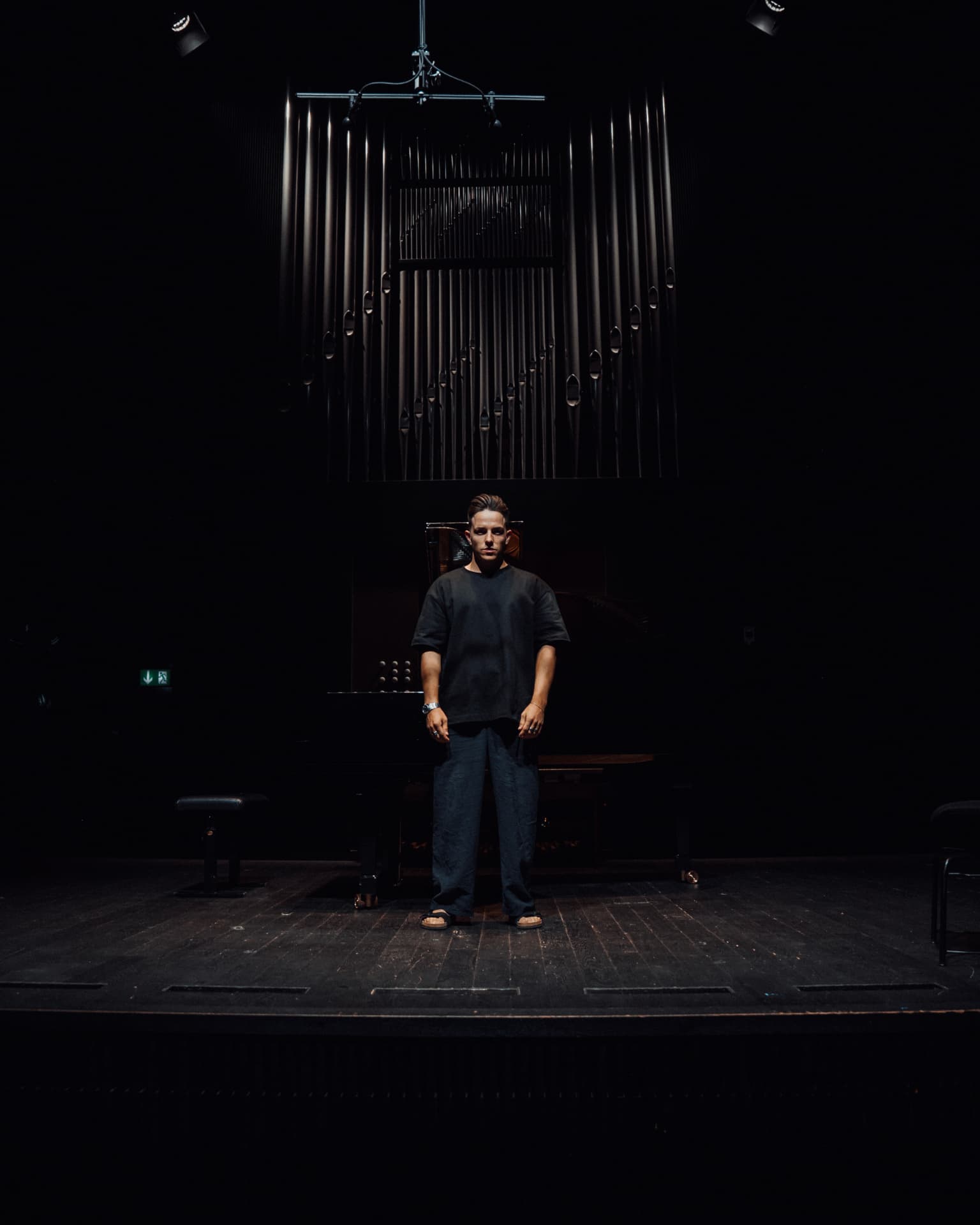 Figure alone on a dark stage beneath organ pipes