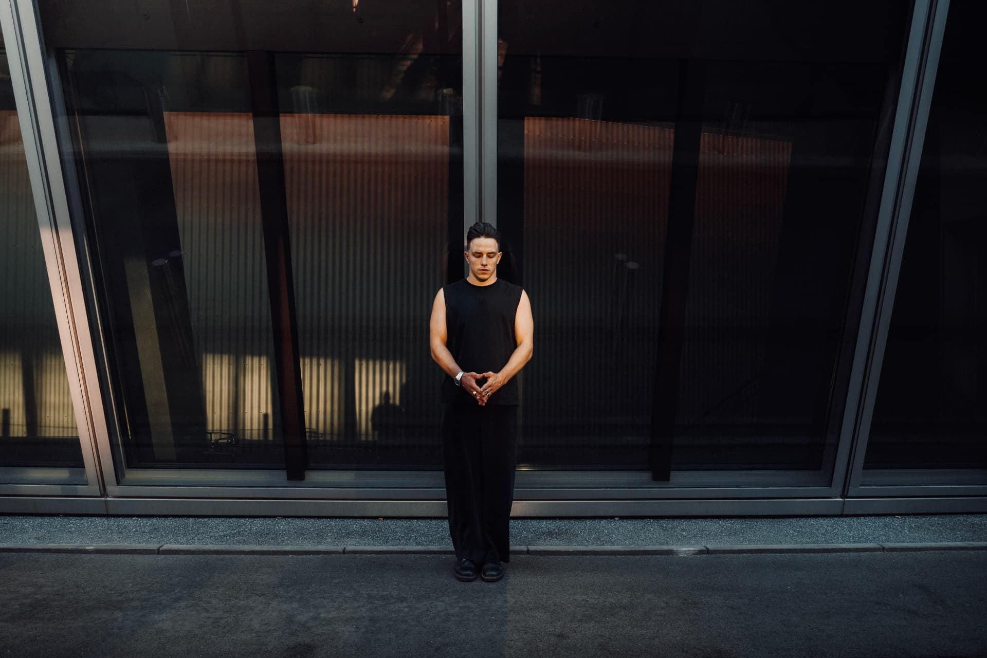 Figure in black standing still before a dark glass facade